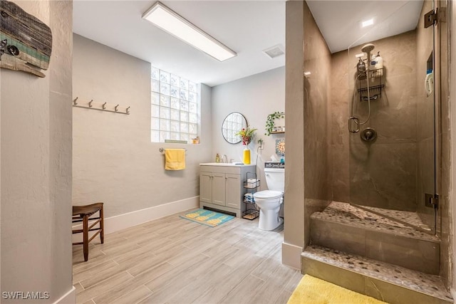 bathroom featuring toilet, vanity, a tile shower, and wood finish floors