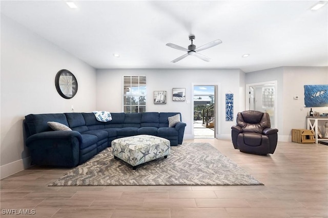 living area with a ceiling fan, light wood-type flooring, and baseboards