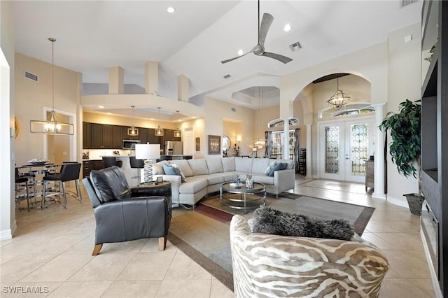 tiled living room with ceiling fan with notable chandelier, a towering ceiling, and french doors