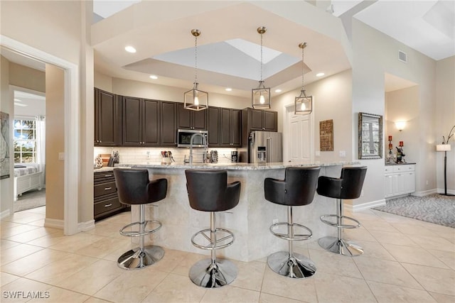 kitchen with a breakfast bar, a spacious island, appliances with stainless steel finishes, a tray ceiling, and decorative light fixtures