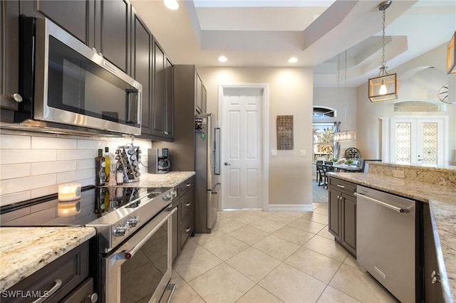 kitchen featuring a tray ceiling, appliances with stainless steel finishes, light stone counters, and pendant lighting