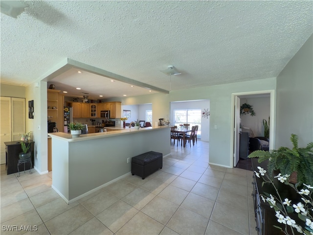 kitchen featuring a textured ceiling, kitchen peninsula, light tile patterned floors, and stainless steel appliances