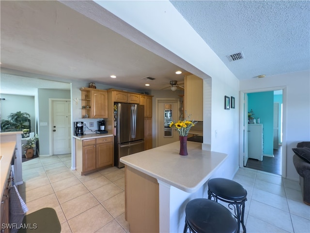 kitchen with a textured ceiling, stainless steel refrigerator, a breakfast bar area, and light tile patterned flooring