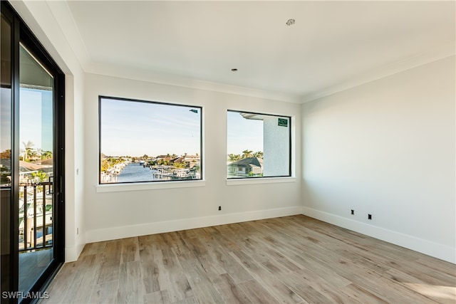 unfurnished room featuring crown molding, a water view, and light wood-type flooring