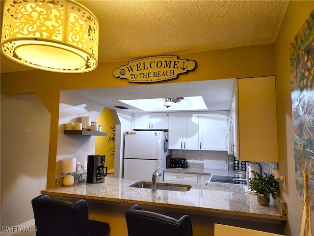 kitchen featuring backsplash, light stone counters, white appliances, sink, and white cabinetry