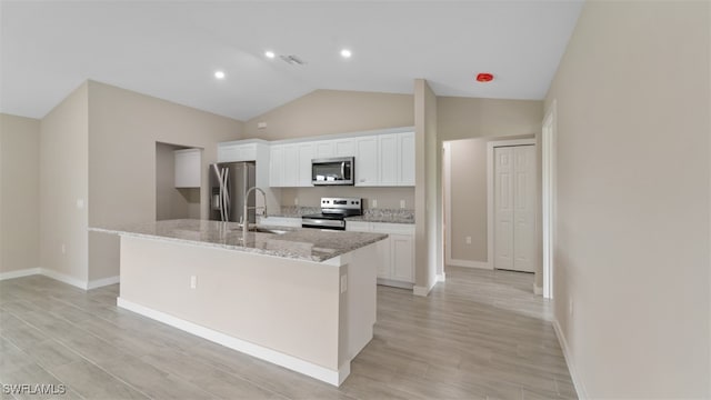 kitchen with a center island with sink, vaulted ceiling, light hardwood / wood-style floors, white cabinetry, and stainless steel appliances