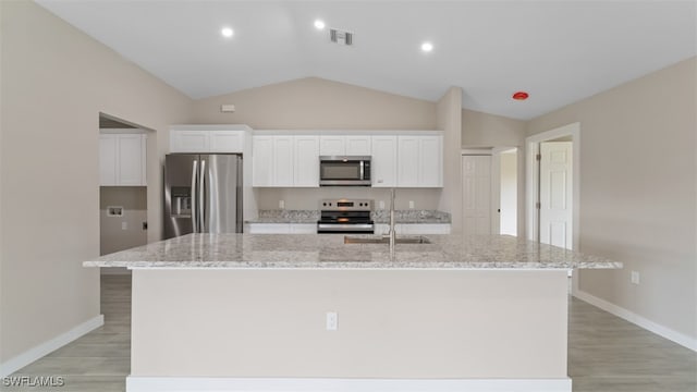 kitchen featuring white cabinets, appliances with stainless steel finishes, vaulted ceiling, and a kitchen island with sink