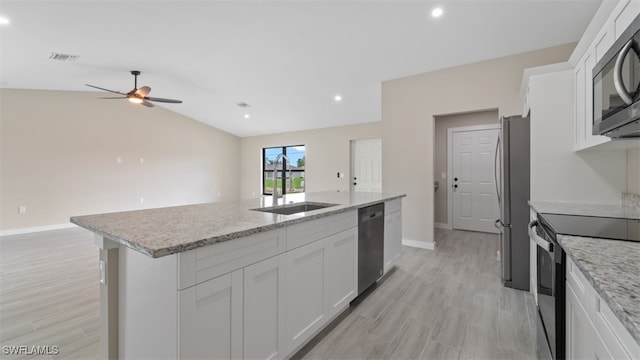 kitchen featuring sink, lofted ceiling, a center island with sink, white cabinets, and appliances with stainless steel finishes