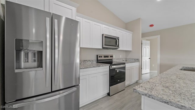 kitchen featuring appliances with stainless steel finishes, white cabinetry, lofted ceiling, and light stone counters