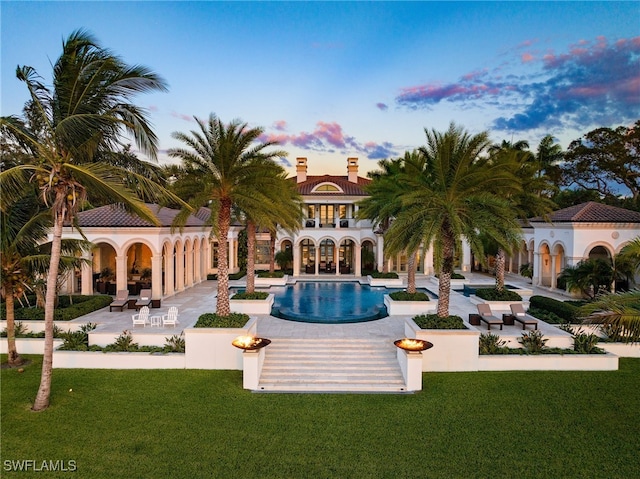 pool at dusk with a patio and a lawn