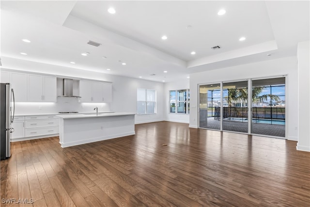 kitchen featuring a center island with sink, wall chimney exhaust hood, dark hardwood / wood-style floors, and white cabinets