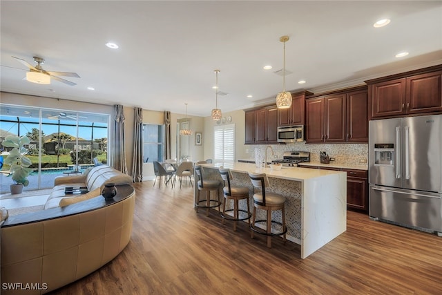 kitchen featuring a breakfast bar, a center island with sink, hanging light fixtures, dark hardwood / wood-style floors, and stainless steel appliances