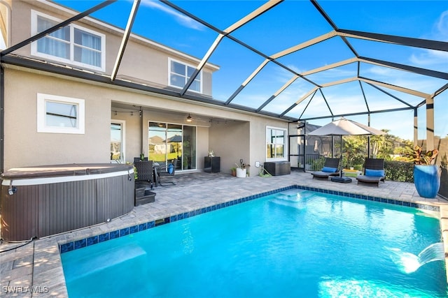 view of pool featuring glass enclosure, ceiling fan, a patio, and a hot tub