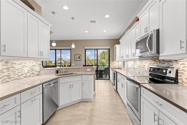 kitchen with appliances with stainless steel finishes, ornamental molding, sink, decorative light fixtures, and white cabinetry