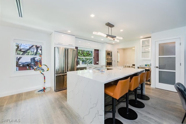 kitchen with light stone countertops, appliances with stainless steel finishes, light wood-type flooring, pendant lighting, and white cabinets