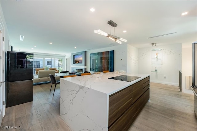 kitchen featuring light stone countertops, a center island, hanging light fixtures, light hardwood / wood-style floors, and black electric stovetop