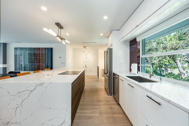 kitchen with light stone countertops, appliances with stainless steel finishes, sink, white cabinets, and light hardwood / wood-style floors