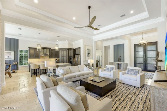 living room with ceiling fan with notable chandelier, ornamental molding, french doors, and a tray ceiling