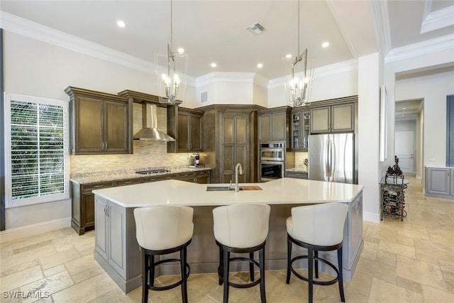 kitchen featuring wall chimney exhaust hood, stainless steel appliances, a spacious island, sink, and hanging light fixtures