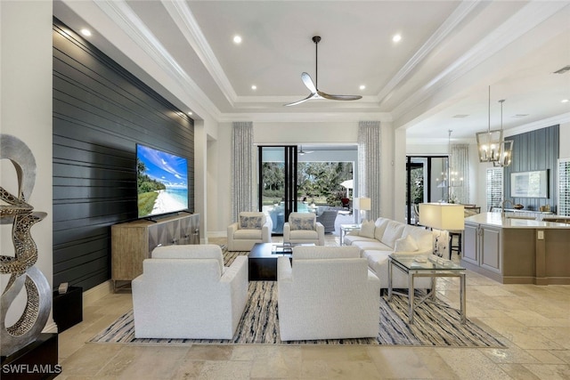 living room with ceiling fan with notable chandelier, a raised ceiling, crown molding, and wood walls