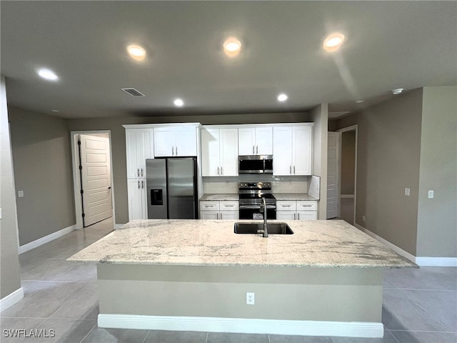 kitchen featuring white cabinets, light tile patterned floors, an island with sink, light stone counters, and stainless steel appliances