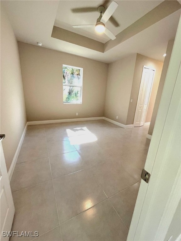 spare room with ceiling fan, light tile patterned flooring, and a tray ceiling