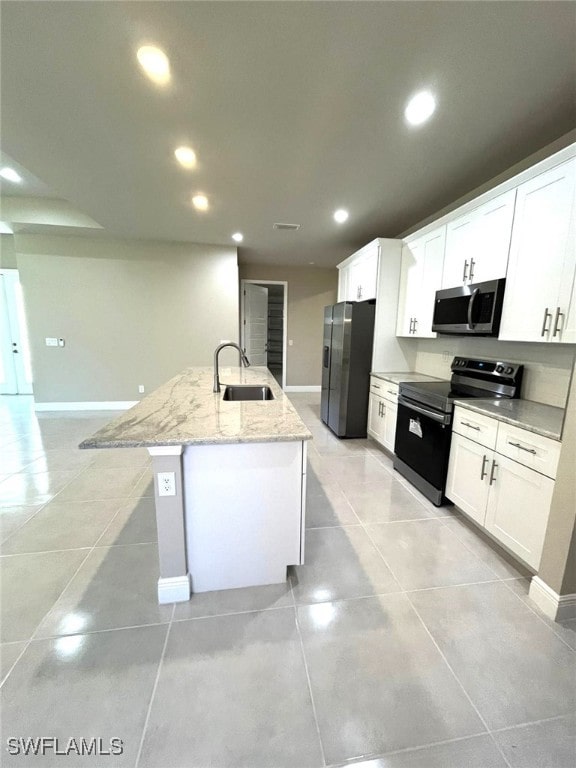 kitchen with sink, an island with sink, appliances with stainless steel finishes, light stone counters, and white cabinetry