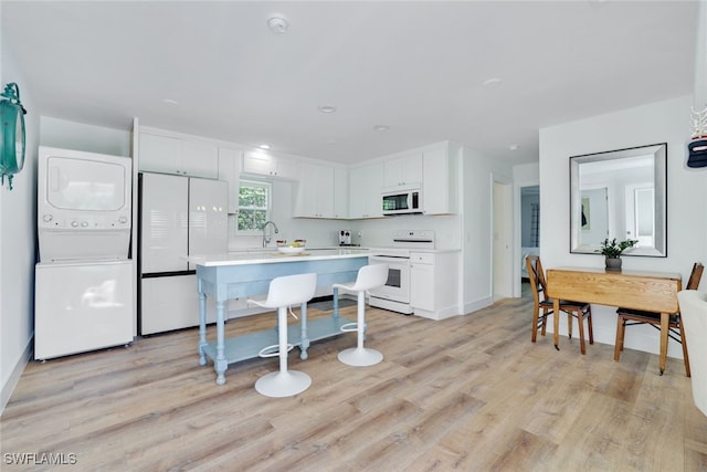 kitchen with white appliances, white cabinets, sink, stacked washing maching and dryer, and light wood-type flooring