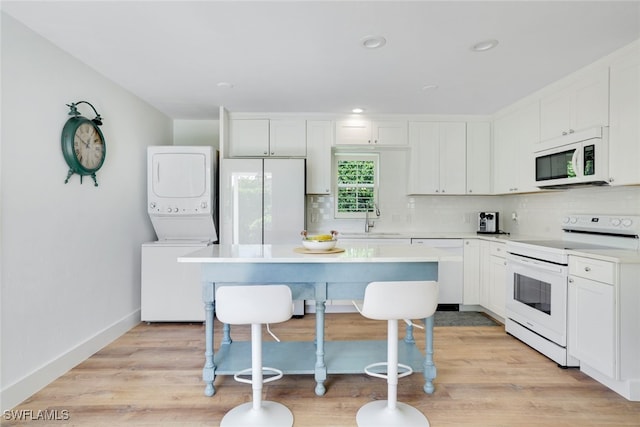 kitchen featuring white cabinetry, stacked washing maching and dryer, white appliances, and light wood-type flooring