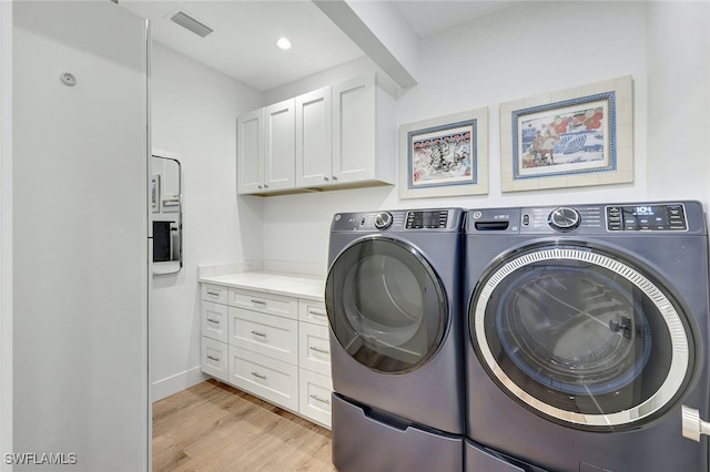 laundry room with cabinets, washer and dryer, and light wood-type flooring