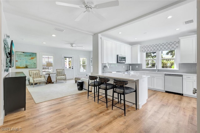 kitchen with light hardwood / wood-style floors, white cabinets, a healthy amount of sunlight, and appliances with stainless steel finishes