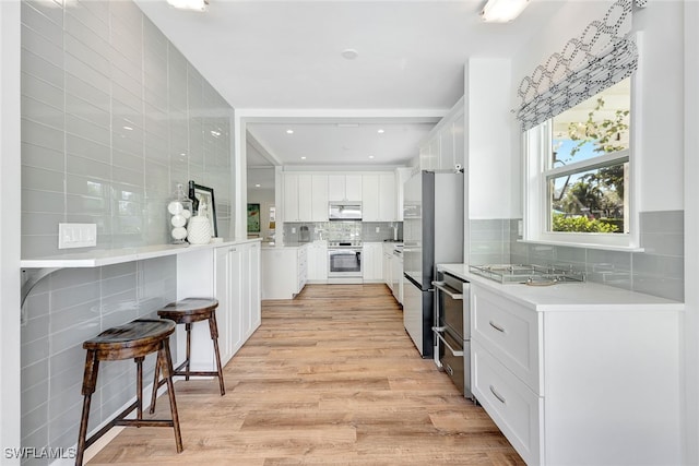 kitchen featuring light hardwood / wood-style flooring, backsplash, stainless steel fridge, white cabinets, and range