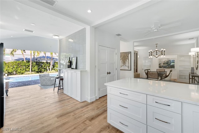 kitchen featuring ceiling fan, a breakfast bar area, light hardwood / wood-style floors, white cabinetry, and lofted ceiling