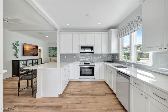 kitchen featuring white cabinets, a kitchen breakfast bar, sink, appliances with stainless steel finishes, and light hardwood / wood-style floors