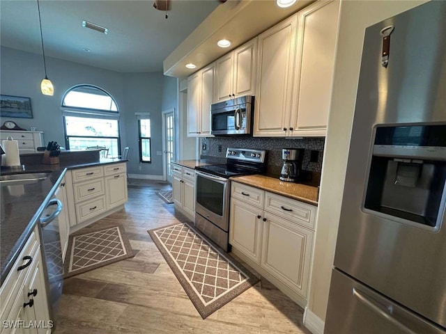 kitchen with decorative backsplash, light wood-type flooring, stainless steel appliances, sink, and hanging light fixtures