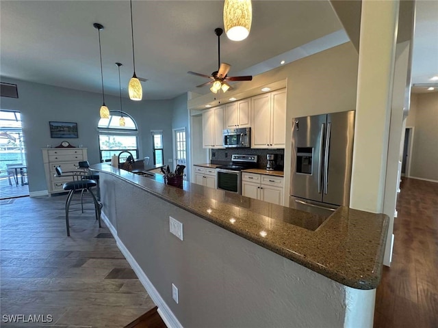 kitchen with dark hardwood / wood-style flooring, stainless steel appliances, pendant lighting, dark stone countertops, and white cabinets