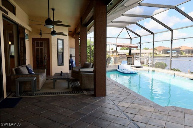 view of swimming pool featuring a water view, ceiling fan, a lanai, a patio area, and exterior kitchen