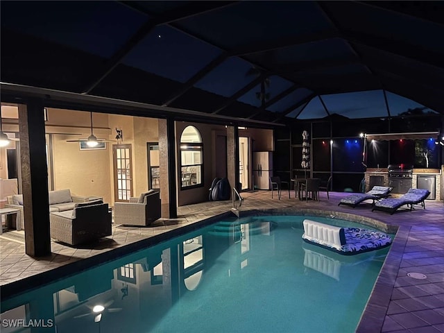 pool at night featuring glass enclosure, a grill, an outdoor living space, a patio area, and area for grilling