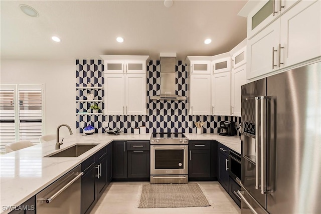 kitchen featuring light stone counters, wall chimney exhaust hood, stainless steel appliances, sink, and white cabinets