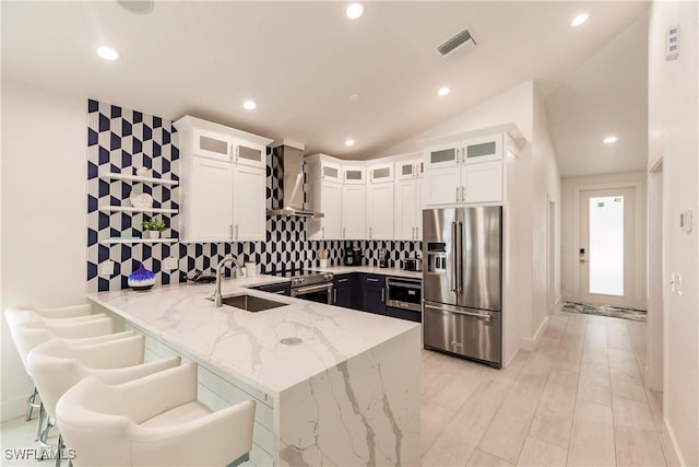 kitchen with sink, stainless steel appliances, wall chimney range hood, light stone counters, and decorative backsplash