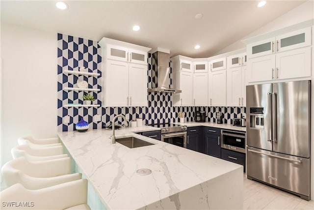 kitchen with kitchen peninsula, appliances with stainless steel finishes, light stone counters, wall chimney range hood, and white cabinetry