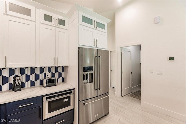 kitchen featuring light wood-type flooring, tasteful backsplash, light stone counters, white cabinetry, and stainless steel appliances