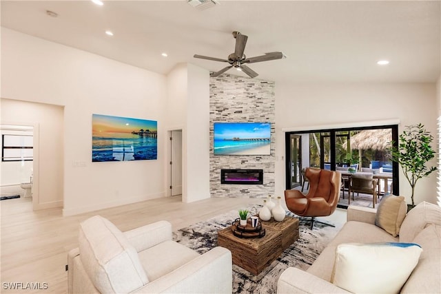 living room featuring ceiling fan, light hardwood / wood-style floors, a stone fireplace, and high vaulted ceiling