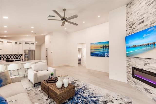 living room with ceiling fan, a fireplace, high vaulted ceiling, and light hardwood / wood-style floors