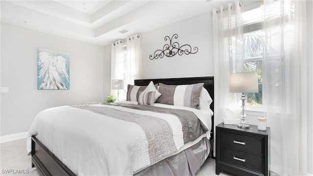 bedroom featuring visible vents, multiple windows, baseboards, and a tray ceiling