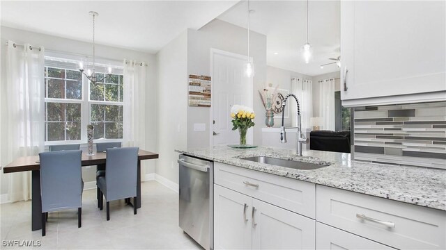 kitchen featuring tasteful backsplash, light stone counters, stainless steel dishwasher, pendant lighting, and a sink