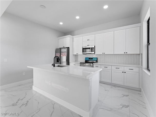 kitchen featuring white cabinets, backsplash, a kitchen island with sink, and appliances with stainless steel finishes