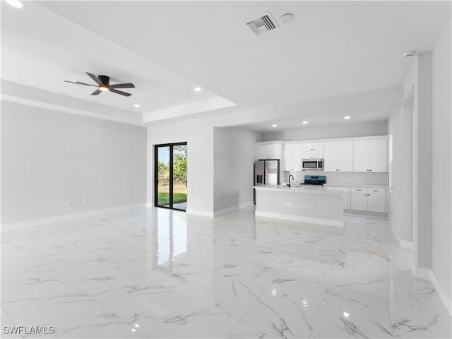 unfurnished living room featuring a raised ceiling, ceiling fan, and sink