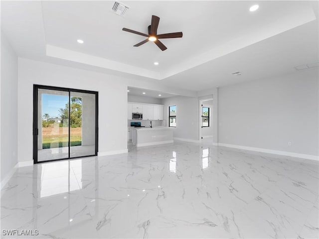 unfurnished living room featuring ceiling fan and a tray ceiling