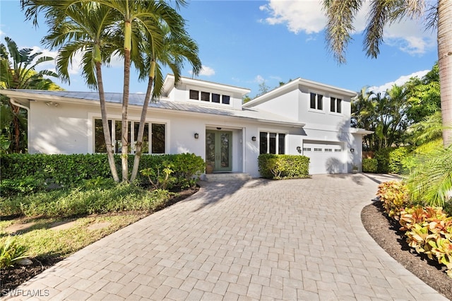 traditional home with stucco siding, an attached garage, decorative driveway, and french doors